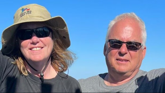 Un homme et une femme se photographient, la femme portant un chapeau et des lunettes noires tandis que les yeux de l'homme sont couverts de lunettes noires.