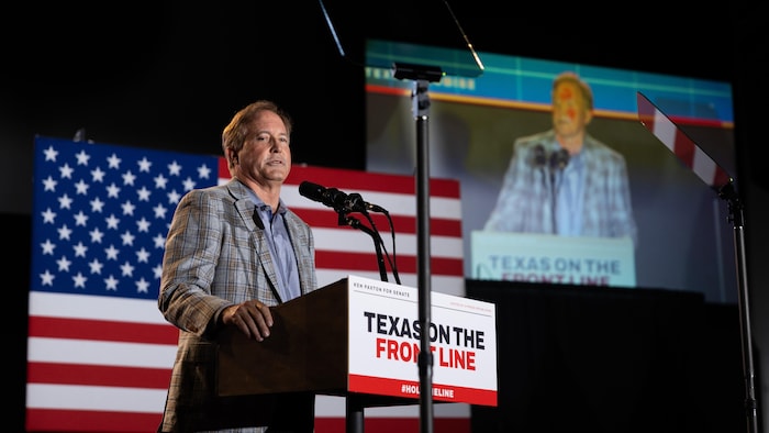 Ken Paxton parle derrière un lutrin. Un drapeau américain est projeté derrière lui.