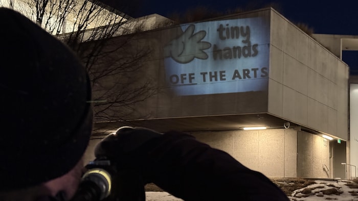Un homme projette une image sur un mur à l'aide d'une lampe.
