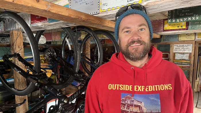 Kenneth Sanderson sourit à la caméra. Des vélos sont accrochés en arrière de lui.