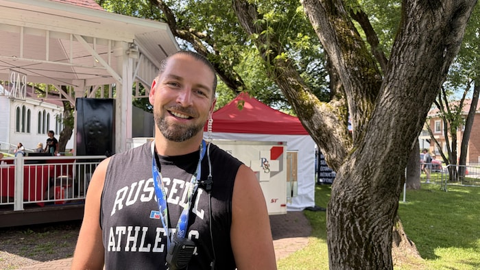 Un homme souriant portant un chandail sans manches et un récepteur radio pose au premier plan.