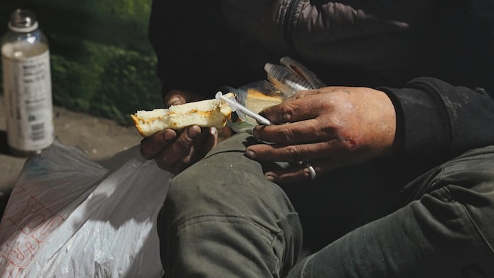 Un homme mange un sandwich en tenant une seringue dans le quartier de Kensington à Philadelphie.