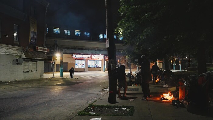 Le métro de Philadelphie traverse le quartier de Kensington près d'un parc surnommé le parc des aiguilles, pendant la nuit. Des dizaines de personnes y consomment de la drogue et se réchauffent près de feux de camp.