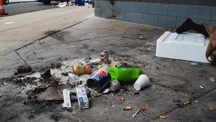 Un sans-abri dort devant une station de métro du quartier Kensington, à Philadelphie. Des déchets, une seringue et les résidus d'un feu de camp traînent tout près.