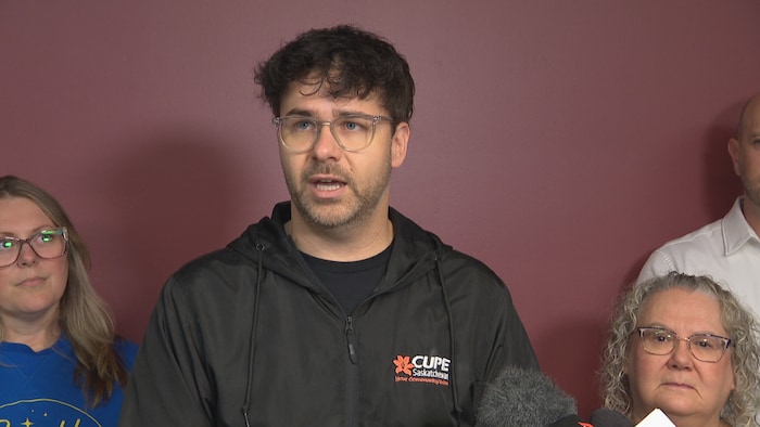 Kent Peterson  du Syndicat canadien de la fonction publique en Sastachewan debout devant un pupitre pour faire son discours devant les journalistes. 