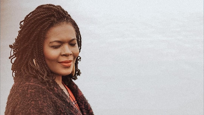 Kettly Excellent, les yeux fermés. En arrière-plan, les eaux grises d'un lac scintille.