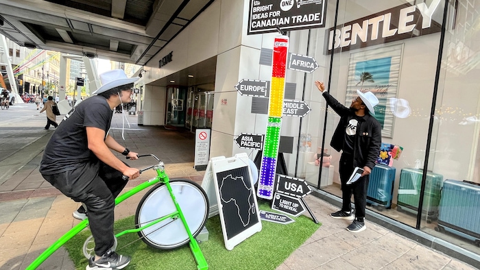 Un homme pédale sur un vélo stationnaire pour allumer une tour électrique à côté de laquelle se tient un autre homme.