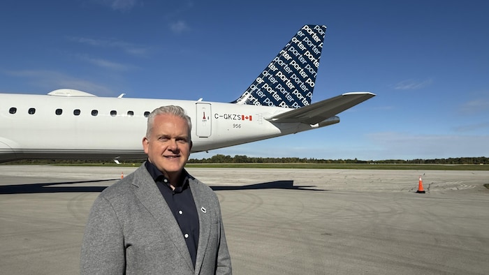 Kevin Jackson, président de Porter Airlines, pose sur le tarmac devant un avion de la compagnie aérienne, dont on aperçoit la queue ornée du logo Porter.