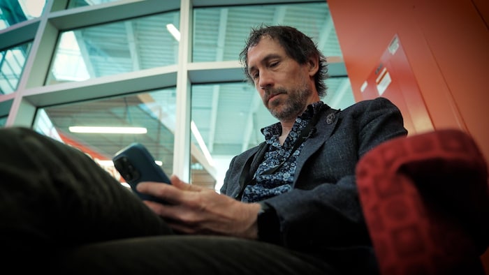Un homme assis regarde son téléphone cellulaire.