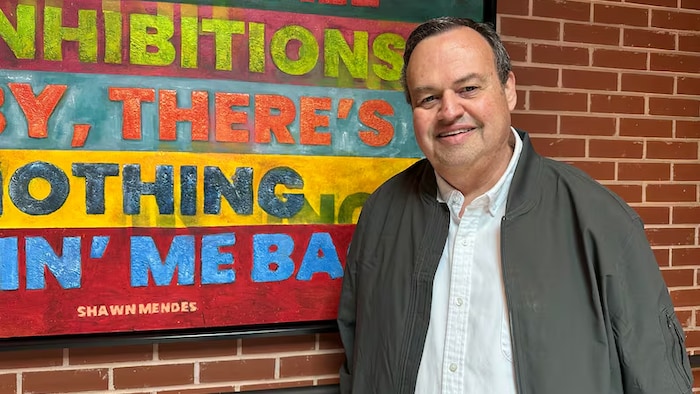 Kevin Morrison devant une enseigne peinte sur un mur de brique.