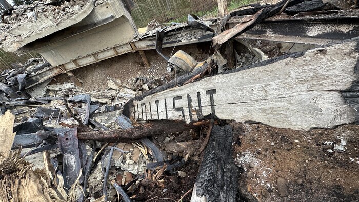 Photo d'un morceau de bois brulé, sur les restes d'un bâtiment.