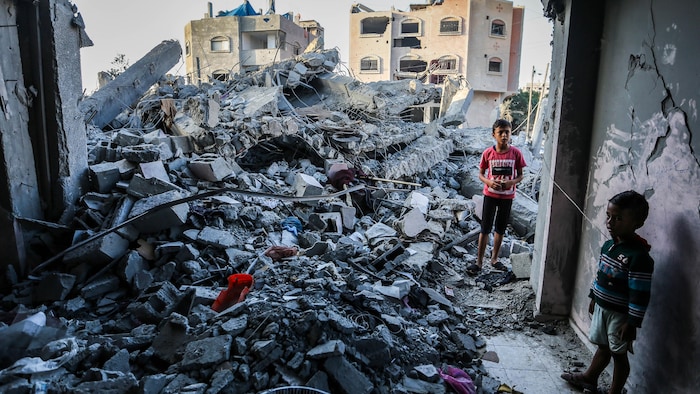 Deux enfants debout dans les ruines d'un immeuble, la mine triste.