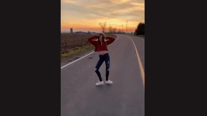 Une jeune femme pratique des mouvements de danse sur une route déserte à la tombée du jour.