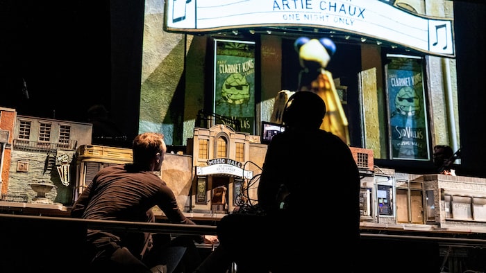 Un écran géant projette une scène de «The Storyville Mosquito». Deux artistes de dos regardent l'écran.