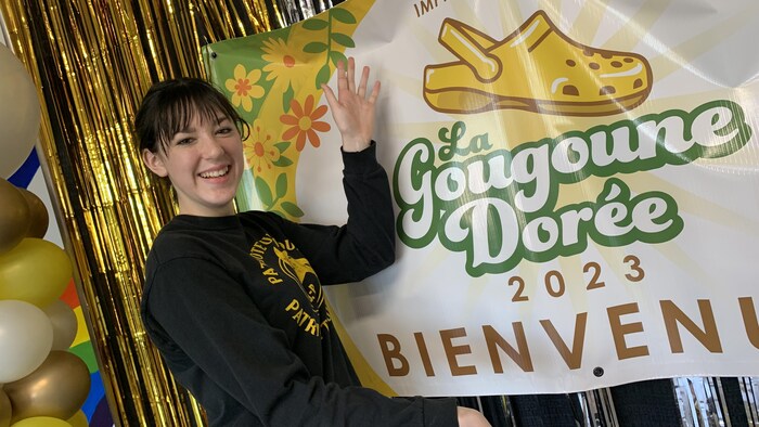 Une adolescente devant une pancarte sur lequel est écrit 'La gougoune dorée 2023' 