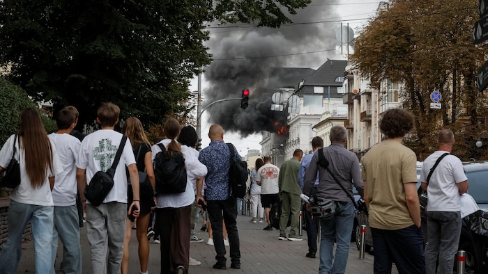 Des passants regarde la fumée qui émane d'un bâtiment.