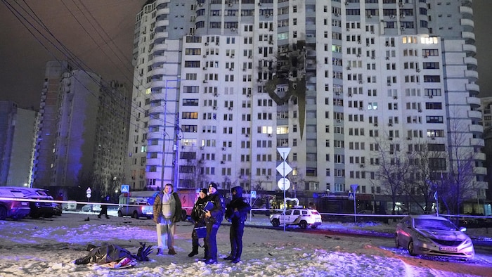 Des policiers se tiennent près d'un corps devant un immeuble d'appartements endommagé après une frappe russe.