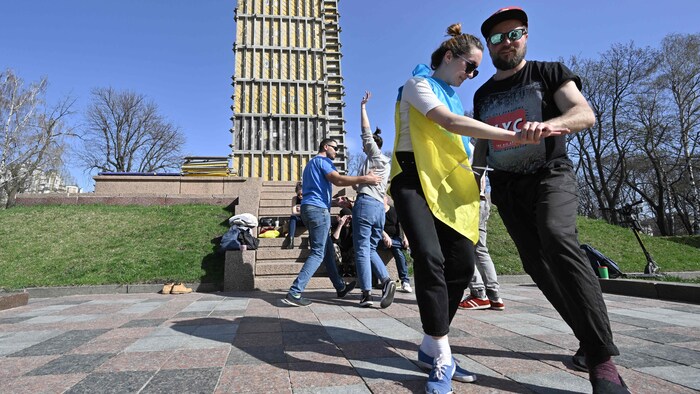 Deux couples dansent sur une place publique.