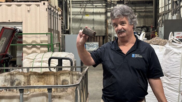 Kim Caron, qu'on voit ici à Calgary, le 2 décembre 2025, montre un boudin de couleur brunâtre devant un grand bac. Le boudin est une briquette de biomasse.
