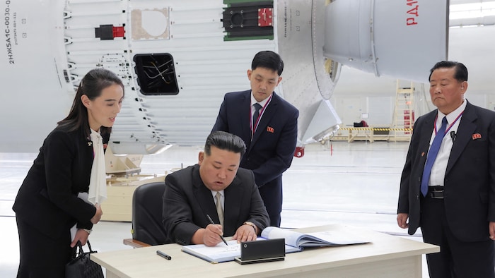 Kim Jong-un assis à une table devant une fusée signe un document.