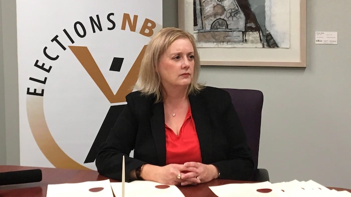Kimberly Poffenroth assise à un bureau devant une affiche d'Élections NB.