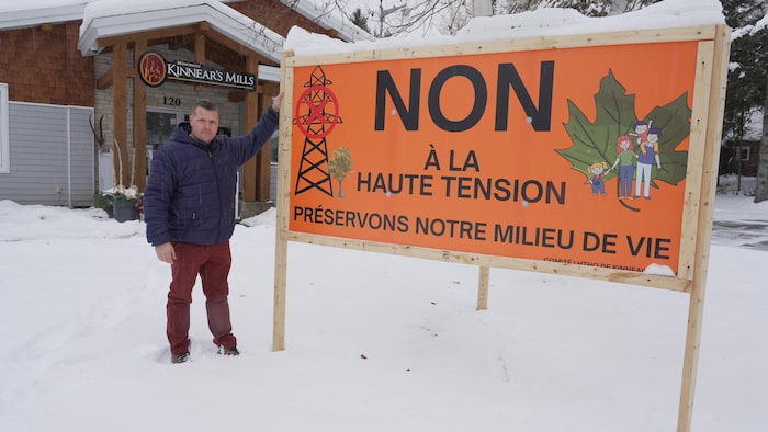 Le maire de Kinnear's Mills s'appuie sur une pancarte en opposition à la ligne à haute tension installée devant l'hôtel de ville.