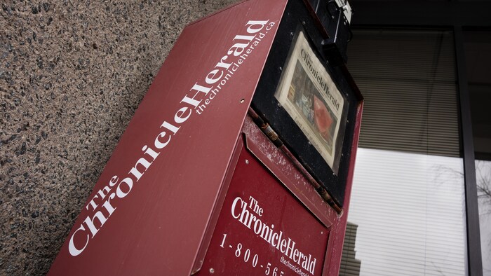 Un distributeur de journaux rouge en métal avec un exemplaire du journal The Chronicle Herald dans le tiroir.