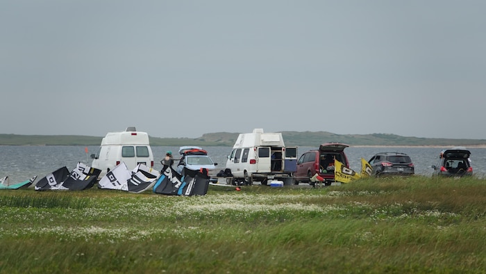 Plusieurs voitures sont garées à proximité d'une lagune avec des voiles de cerf-volant à l'avant-plan.