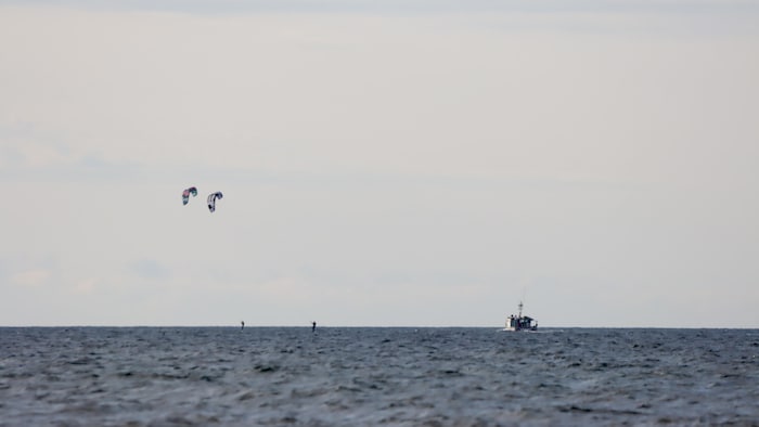 Trois personnes font du kite surf et un bateau sur l'eau