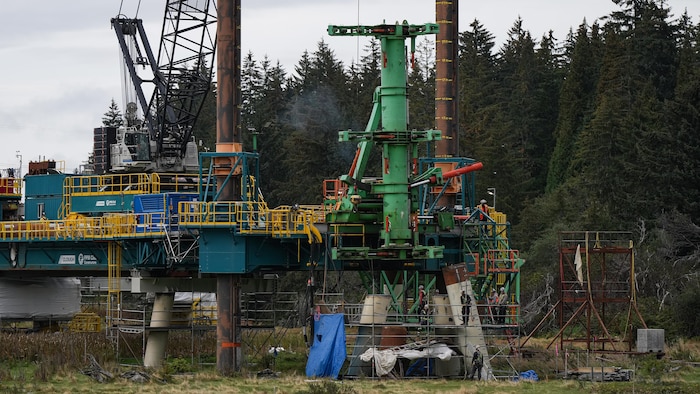Une structure industrielle en acier et du matériel de chantier sont installés près d'une forêt de conifères.