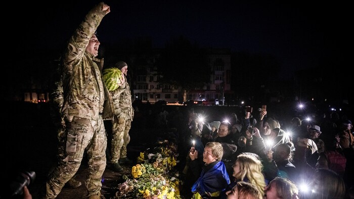 Sur une estrade, Kolya Serga, le poing levé devant la foule, tient une pastèque dans l'autre bras.