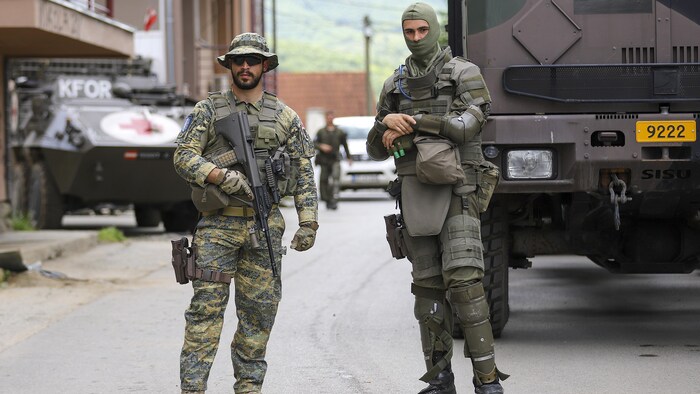 Deux soldats debout devant des véhicules militaires.