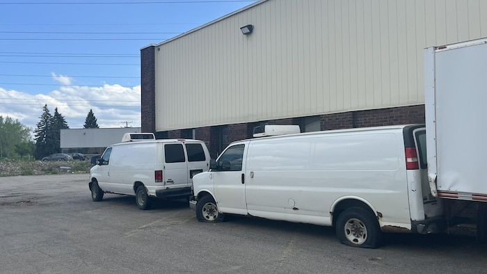 Des véhicules abandonnés devant un entrepôt.