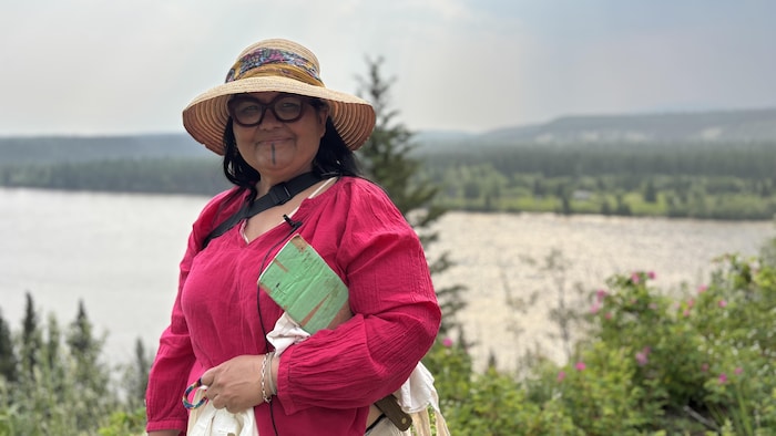 Une femme avec un couteau et un chapeau prend une pose avec la rivière en arrière-plan.