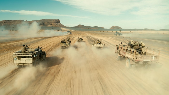 Plusieurs camions de l'armée foncent à toute allure dans un désert. 
