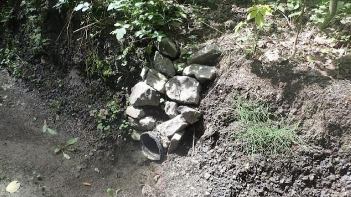 Un détournement de cours d’eau en milieu boisé constitué d’un tuyau en plastique maintenu à l’aide de pierres.