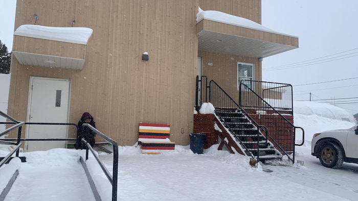 Une femme est assise à l'extérieur à quelques pas de l'entrée de La Piaule, à Val-d'Or