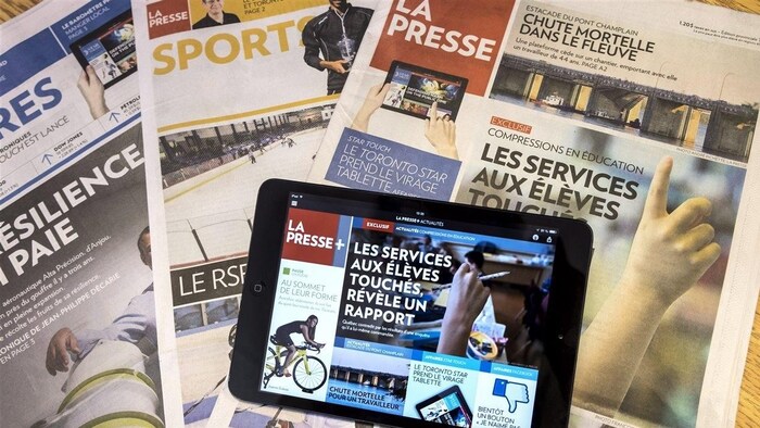 Une tablette montrant la une de La Presse+ est posée sur des cahiers de l'édition papier de La Presse.