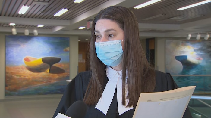 Une avocate en toge portant un masque.