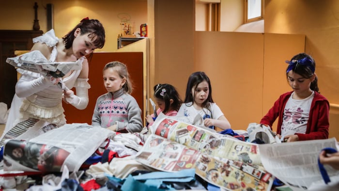 Quatre jeunes filles font du bricolage avec du papier journal, en suivant les instructions d'une femme. 