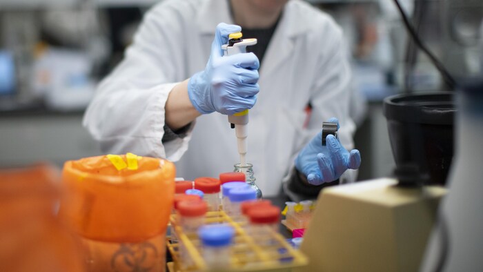 Un homme portant une blouse blanche et des gants de protection travaille dans un laboratoire.
