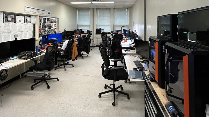Photo d'un bureau plus long que large aux murs couleur crème. De chaque côté, des écrans d'ordinateur et deux imprimantes 3D.