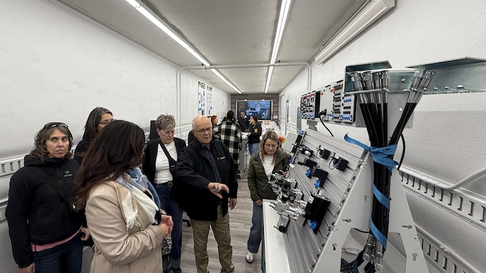 Des gens observent un tableau avec des composantes électroniques dans un laboratoire mobile.