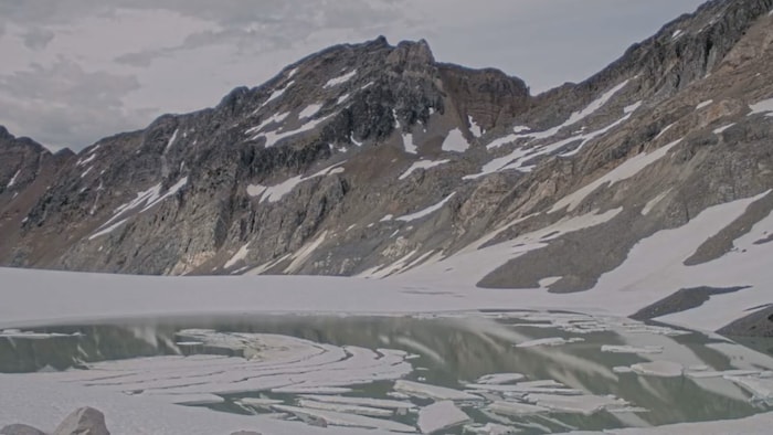 Un lac glaciaire en montagne aux eaux partiellement couvertent de glace.