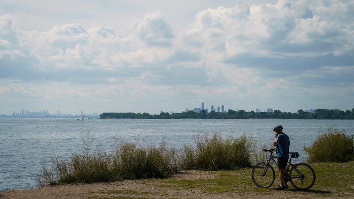 Un cycliste téléphone tout en contemplant le lac Ontario depuis le parc Tommy Thompson, à Toronto, le mardi 25 août 2026.