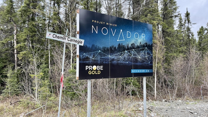 Une affiche du projet minier Novador à l'intersection d'un chemin en forêt.
