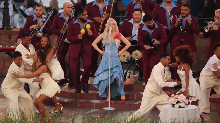 Une femme chante entourée de danseurs et d'un petit orchestre.
