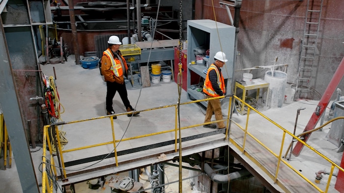 Deux hommes, portant vestes et chapeaux de sécurité, inspectent une usine.