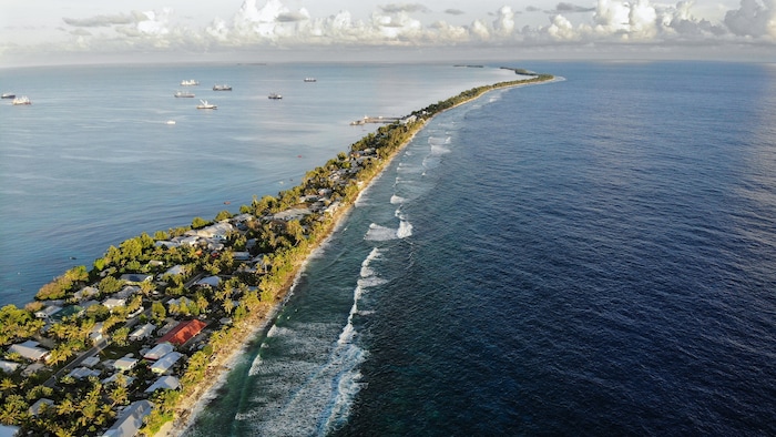  Vue aérienne d'une bande de terre entre l'océan Pacifique et le lagon à Funafuti. À marée haute, l'eau de mer s'infiltre parfois à travers le sol corallien poreux de Tuvalu. Cette nation insulaire du Pacifique Sud, située en zone de faible altitude et comptant environ 11 000 habitants, a été classée comme « extrêmement vulnérable » au changement climatique par le Programme des Nations unies pour le développement. 