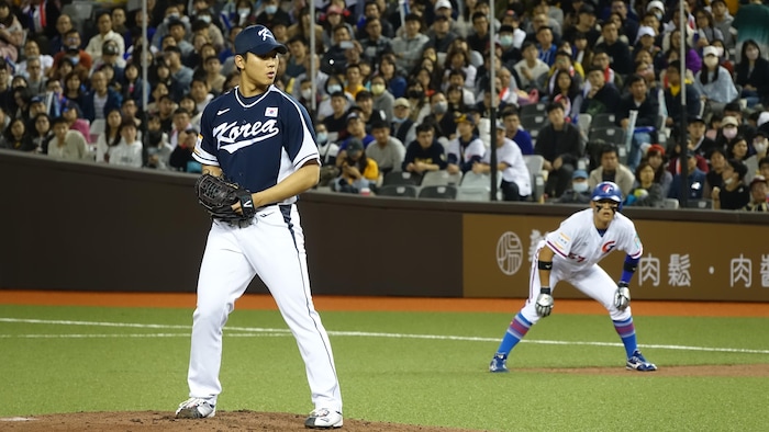 Un lanceur marque une pause tandis qu'on voit un coureur au premier but derrière lui, pendant un match de baseball au Taipei Dome.